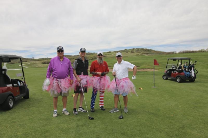 Four golfers in pink tutus, one in stars-and-stripes pants, pose on the course at the Douglas County Veterans Golf Tournament