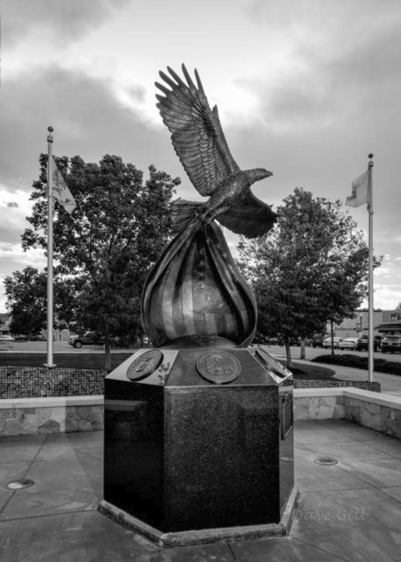 Freedom’s Keeper: a bronze eagle rising from a draped flag atop a black granite pedestal, with flags flying behind it